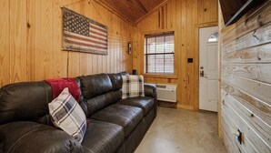 Un intérieur en bois avec un canapé en cuir, un drapeau américain, une fenêtre avec des stores et une porte.