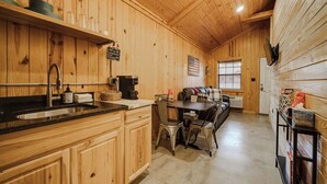 L’intérieur d’un chalet en bois comprend un coin cuisine équipé d’un évier, d’une machine à café et d’une table à manger avec des chaises.