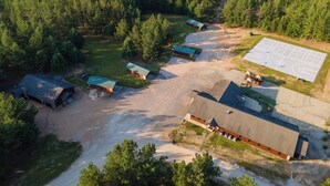 Vue aérienne d’une propriété rurale comprenant plusieurs chalets, un grand bâtiment et un terrain de sport.