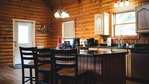 A wooden cabin interior with a kitchen area, a dining table with chairs, and a bar counter. - Timber Lodge Ranch - The Ranch (Amity)