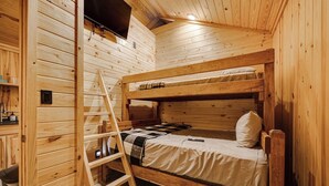 Une pièce de cabane en bois avec des lits superposés, une échelle et une petite étagère sur laquelle se trouve une bouilloire.