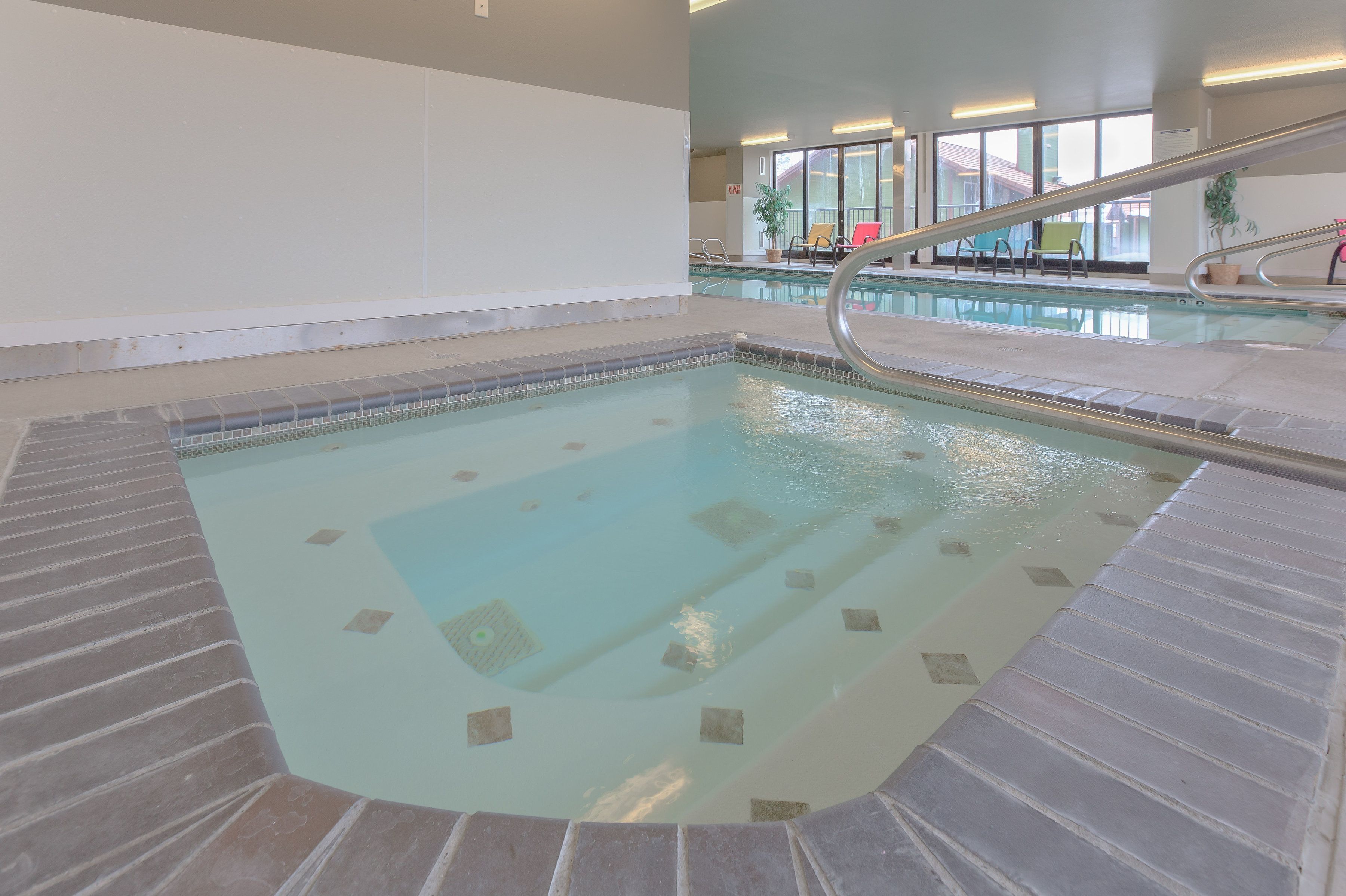 An indoor swimming pool with a tiled deck, a slide, and a view of the outside through large windows.