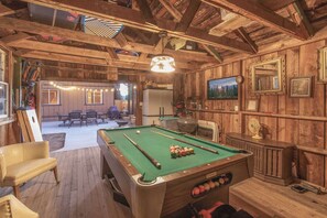 Un tavolo da biliardo in una stanza rustica con pareti e soffitto in legno, una ventola e un televisore appeso al muro.