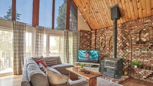 Ein gemütliches Wohnzimmer mit einer Couch, einem Fernseher, einem Kamin und großen Fenstern.