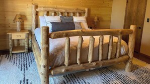 A log cabin-style bedroom with a wooden bed, a nightstand, a lamp, and a ceiling fan. - The BEST VIEW, Rustic Retreat with Hot Tub, Private Fenced Yard, 3BR in Upper Moonridge! (Big Bear City)