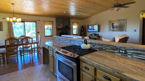 A spacious kitchen with a large island, wooden ceiling, and a stone fireplace. - The BEST VIEW, Rustic Retreat with Hot Tub, Private Fenced Yard, 3BR in Upper Moonridge! (Big Bear City)