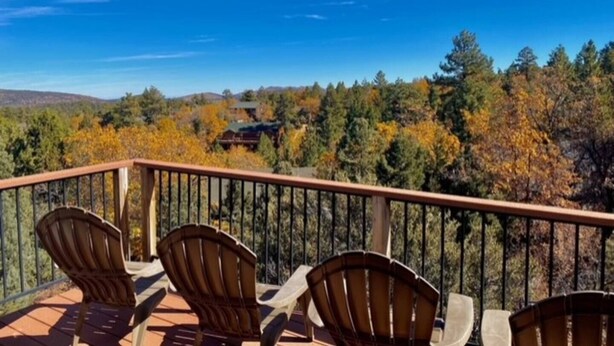 A balcony with wooden chairs and a view of autumn trees and a house in the background. - The BEST VIEW, Rustic Retreat with Hot Tub, Private Fenced Yard, 3BR in Upper Moonridge! (Big Bear City)