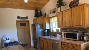 A kitchen with wooden cabinets, a stainless steel refrigerator, a microwave, and a gas stove. - The BEST VIEW, Rustic Retreat with Hot Tub, Private Fenced Yard, 3BR in Upper Moonridge! (Big Bear City)