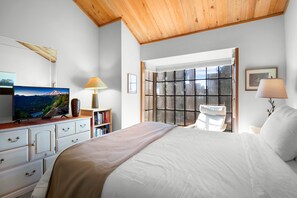 Une chambre à coucher avec un lit, une télévision, une bibliothèque, une fenêtre donnant sur un beau paysage et un plafond en bois.