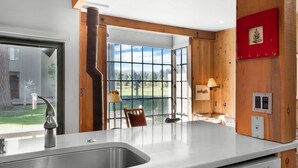 A modern kitchen with a large window, wooden walls, and a view of a green landscape. - Black Butte Ranch Country House 62 (Sisters)