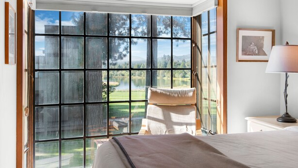 A bedroom with a large window, a bed, a bedside table with a lamp, and a framed picture on the wall. - Black Butte Ranch Country House 62 (Sisters)