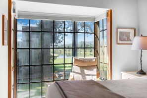 A bedroom with a large window, a bed, a bedside table with a lamp, and a framed picture on the wall. - Black Butte Ranch Country House 62 (Sisters)