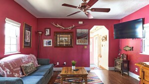 Ein Wohnzimmer mit roter Wand, Deckenventilator, Couchtisch aus Holz, einer Couch und einem Fernseher.