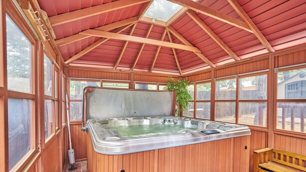 Zona de spa de madera con un jacuzzi, bancos de madera y ventanas grandes.