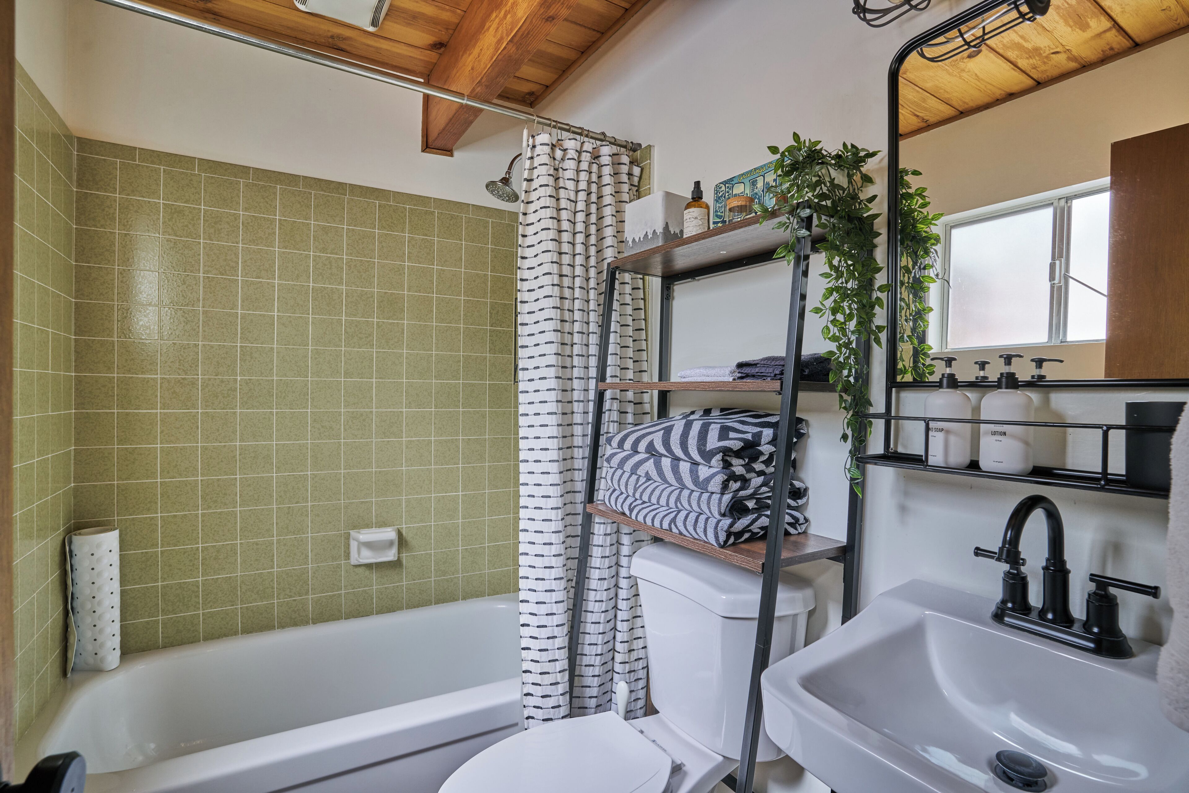 Une salle de bain avec une baignoire, des toilettes et un lavabo. On y trouve un rideau de douche, une étagère avec des articles de toilette et une plante en pot.