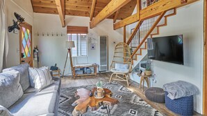 Ein gemütliches Wohnzimmer mit Holzboden, einer Couch, einem Couchtisch, einem Fernseher und einer Treppe.