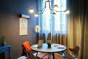 A modern office space with a round table, two chairs, a laptop, a potted plant, a sign on the wall, and a unique ceiling light fixture. - Moxy Brussels City Center (Ixelles)