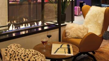 A cozy seating area with a chair, a table, a glass of wine, and a fireplace.