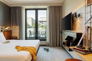 A hotel room with a bed, a TV, a desk with a lamp, and a view of the outside. - Moxy Brussels City Center (Ixelles)