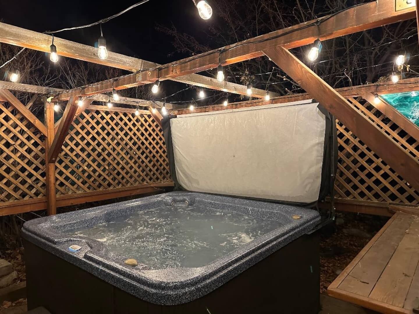 A hot tub with a wooden deck and lattice panels, surrounded by string lights.