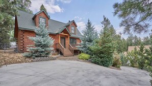 A log cabin with a covered front porch, a driveway, and surrounding evergreen trees. - Peaceful Rustic Escape, Cool Deck with Firepit Table - No Better Escape than Our Private Lot - 3BR w/Game Loft, Pac Man tabletop games console! (Big Bear)