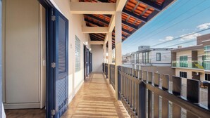 A corridor with a wooden floor, blue doors, and a balcony with a view of buildings.
