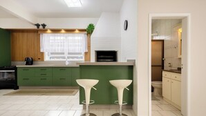 A modern kitchen with a built-in oven, green cabinets, a window with sheer curtains, and two white bar stools.