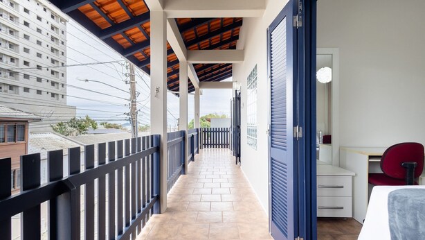A balcony with a tiled floor, a black railing, a blue door, and a red chair.