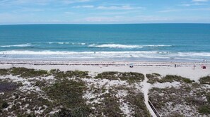 Ein Strand mit freiem Blick auf den Ozean, einem sandigen Pfad und vereinzelter Vegetation.