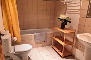 A small bathroom with a toilet, a bathtub, a sink, and a shelf with a potted plant. - Mas de l'Estiou (Monteux)