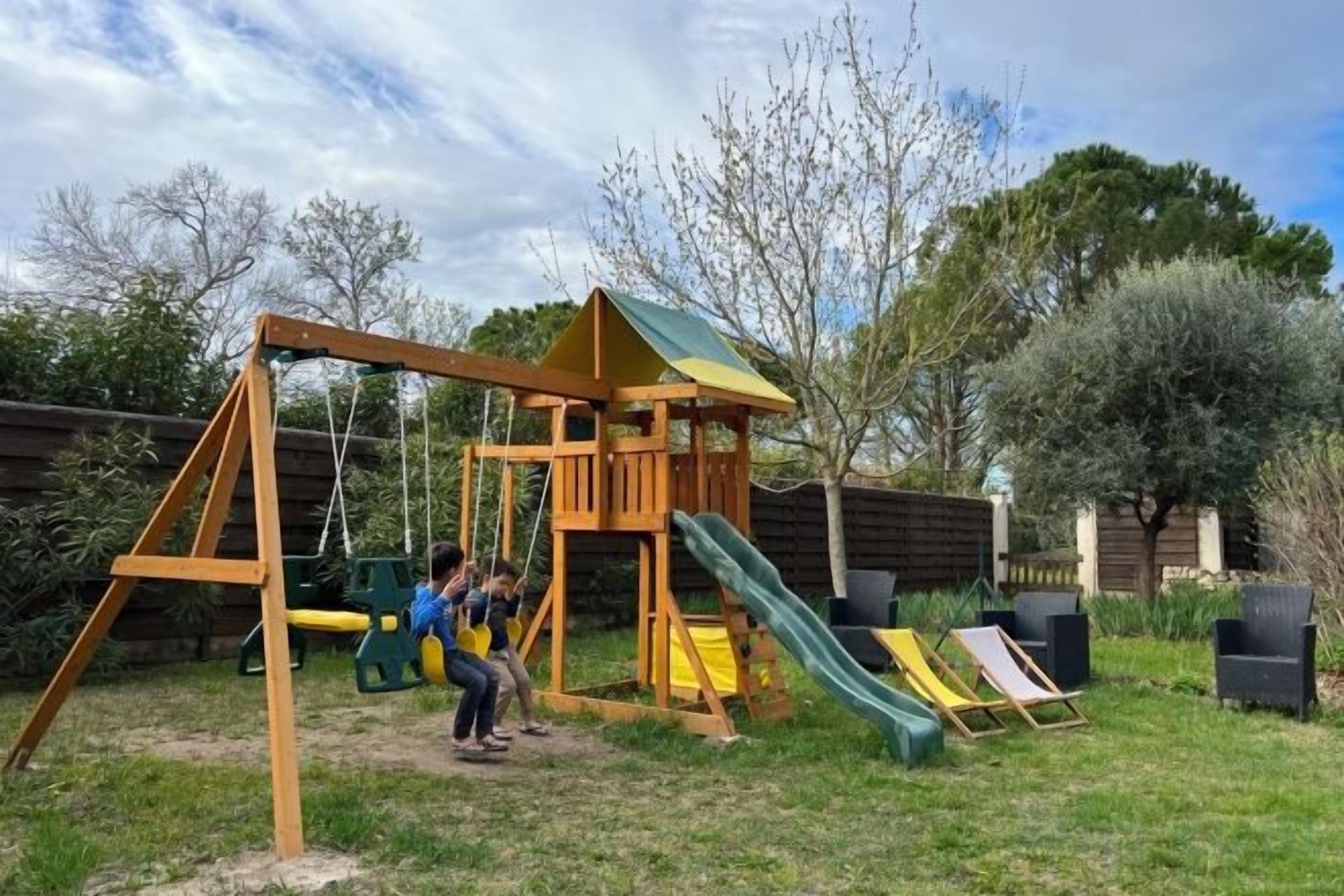 A wooden play structure with a slide and swings in a backyard.