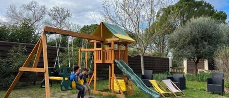 Una estructura de juego de madera con un tobogán y columpios en un patio trasero.