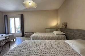 A bedroom with two beds, a window with curtains, a radiator, and a hanging light fixture. - Mas de l'Estiou (Monteux)