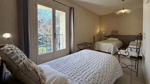 Quarto de hotel com duas camas, janela com cortinas, luminária pendente e cadeira com almofada.