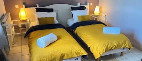 Una habitación con dos camas, cada una con ropa de cama amarilla y almohadas blancas. Hay lámparas de noche en cada mesita.