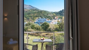 En balkon med bord og stole, der ud til et landsbymiljø med bygninger og bakker.