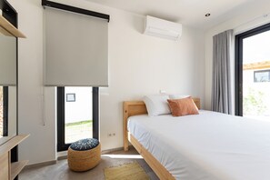Une chambre à coucher comprenant un lit, une fenêtre, un appareil de climatisation et un petit tabouret.