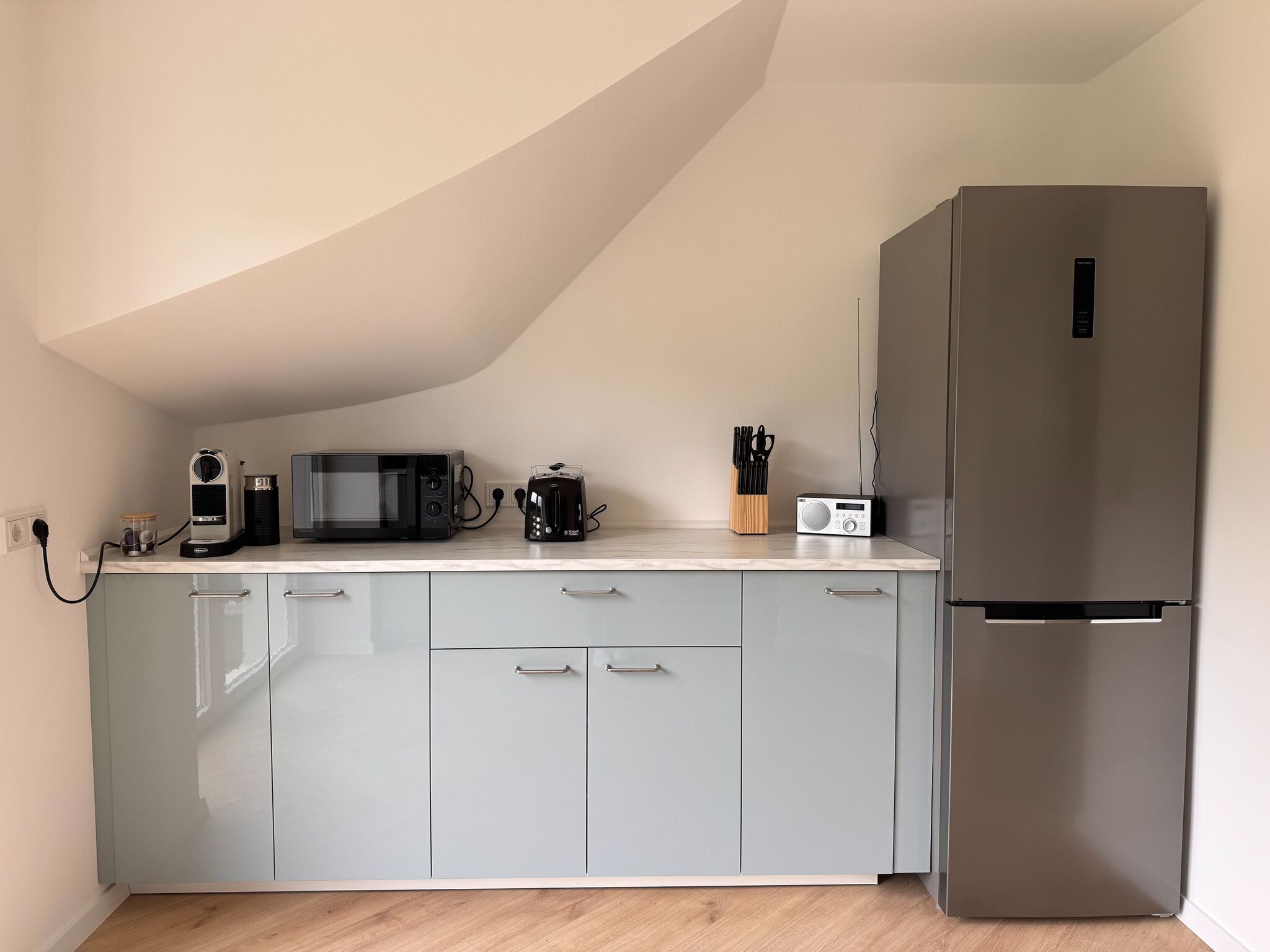 A kitchen with a microwave, toaster, and radio on the counter, a refrigerator, and light grey cabinets.