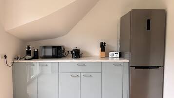 A kitchen with a microwave, toaster, and radio on the counter, a refrigerator, and light grey cabinets.