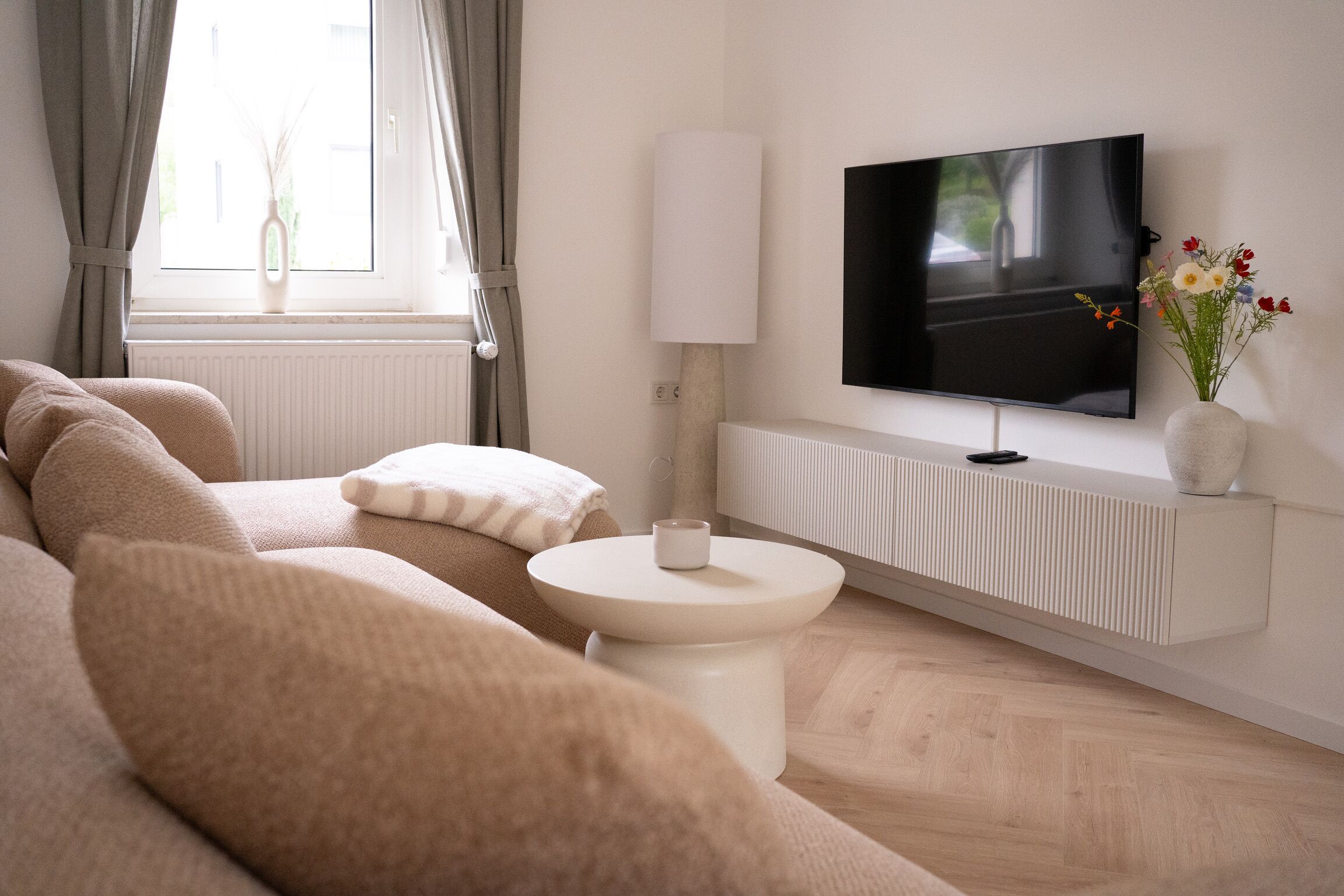 Ein modernes Wohnzimmer mit einer Couch, einem kleinen Beistelltisch, einem flachbildfernseher an der Wand und einer Heizung darunter.