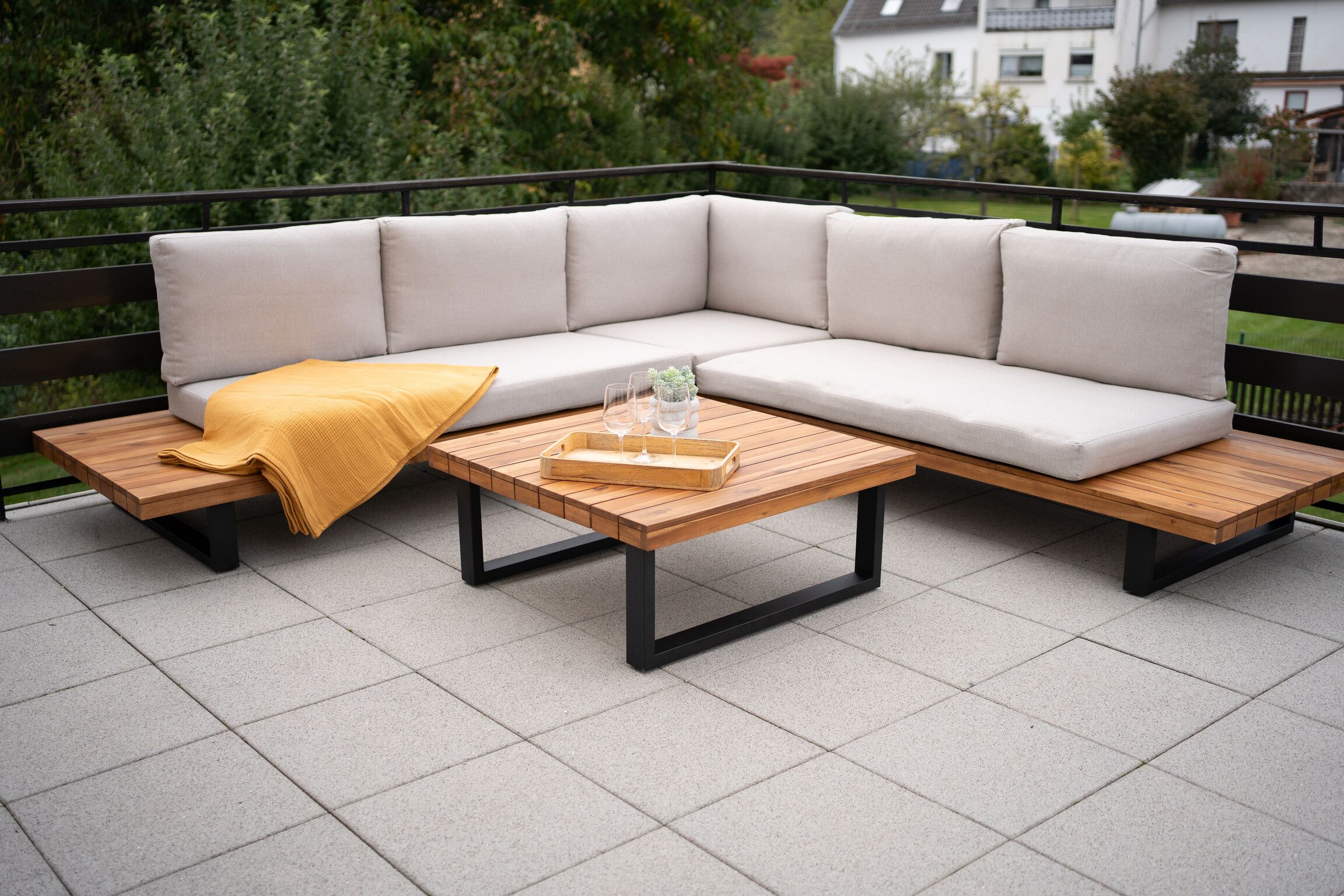 A sectional sofa with cushions, a wooden coffee table, and a yellow throw blanket on a patio with tiled flooring.
