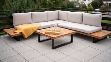 A sectional sofa with cushions, a wooden coffee table, and a yellow throw blanket on a patio with tiled flooring.