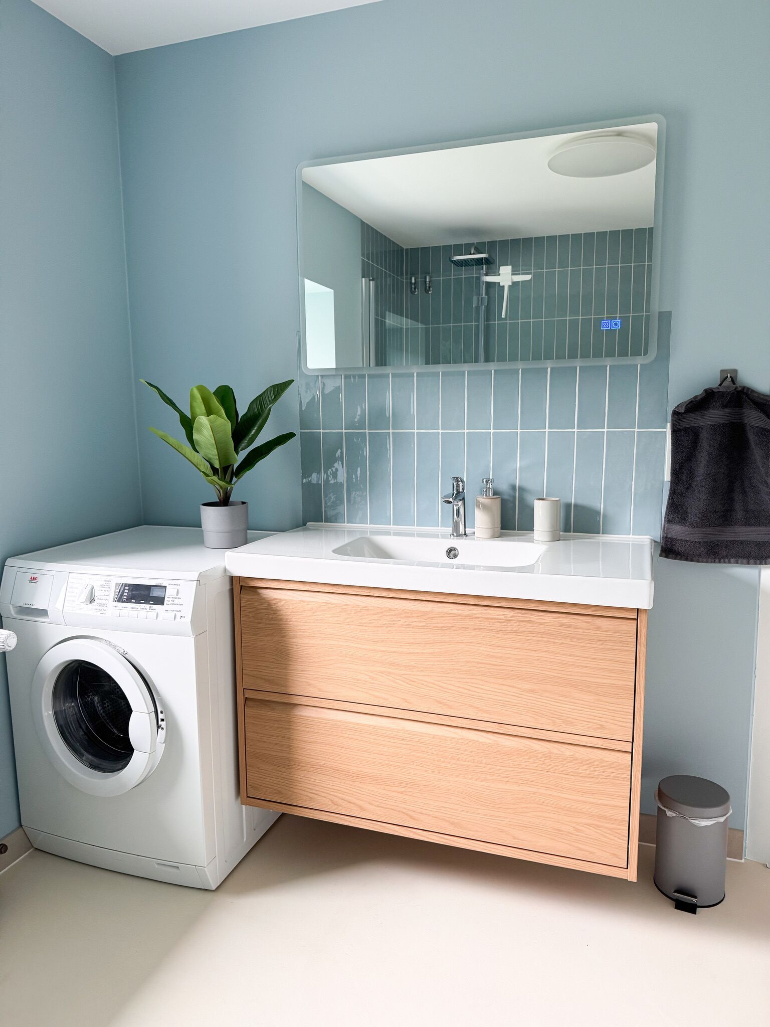 A modern bathroom with a washing machine, a sink, and a mirror.