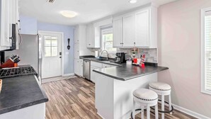 Una cocina moderna con armarios blancos, una isla central con taburetes, un refrigerador de acero inoxidable y una cafetera.