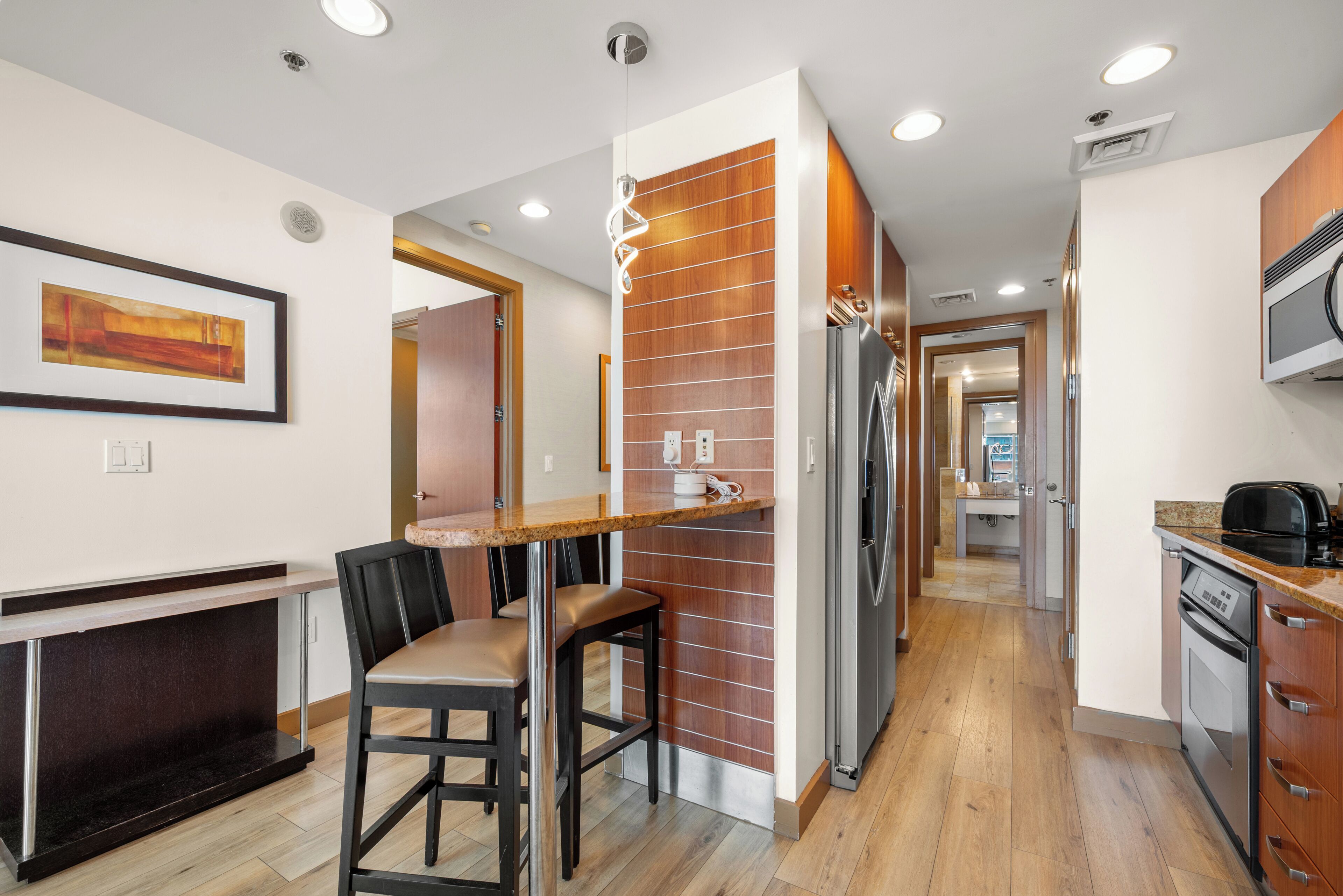 Cocina moderna con una pared decorativa de madera, un refrigerador empotrado y un comedor con un taburete de bar.
