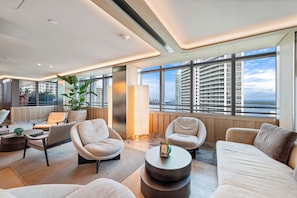 A modern hotel room with a large window, a sofa, a chair, a coffee table, and a plant.