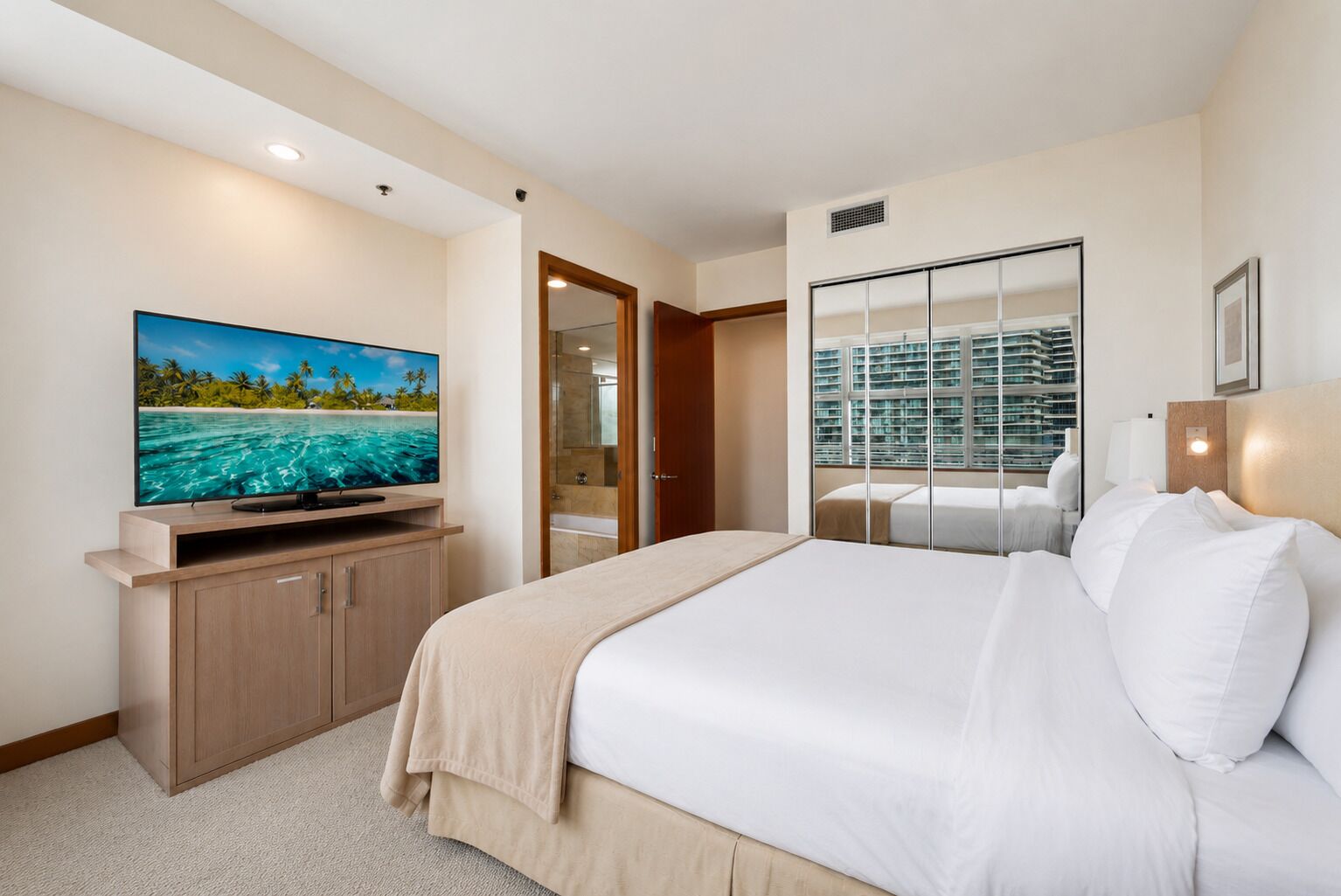 A hotel room with a large bed, a television on a wooden cabinet, a walk-in closet, and a view of a pool and building.