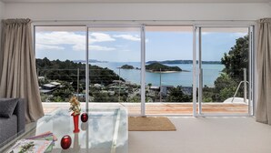 A modern room with a glass table, a red vase, and a view of a coastal landscape. - Seabreeze Sanctuary - Paihia Holiday Home (Paihia)