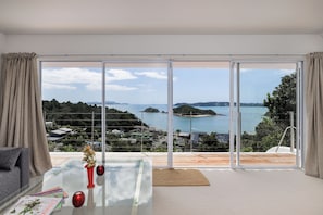 Une chambre moderne avec une table en verre, un vase rouge et une vue sur un paysage côtier.