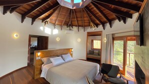 A bedroom with a wooden ceiling, a bed, a chair, and a window with a view of trees. - Atiaia Jungle River Retreat (Bocaina de Minas)